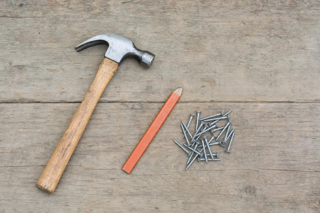 A claw hammer, a flat pencil and loose galvanized screws laid flat on a timber plank seen from above — patio cover, Longview. Illustrative example.